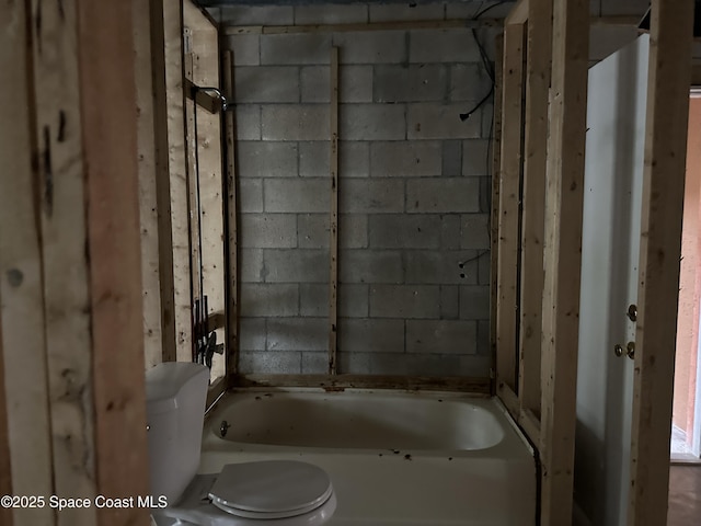 full bath featuring concrete block wall, toilet, and a tub