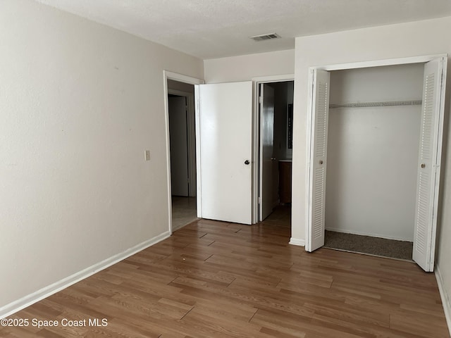 unfurnished bedroom with baseboards, a closet, visible vents, and wood finished floors