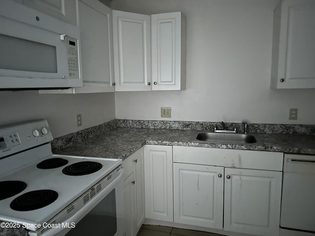 kitchen featuring white appliances, dark countertops, a sink, and white cabinets