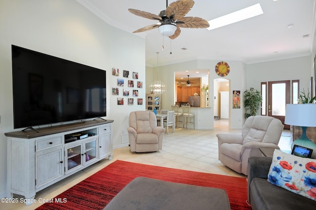 living area featuring vaulted ceiling with skylight, arched walkways, a ceiling fan, ornamental molding, and light tile patterned flooring