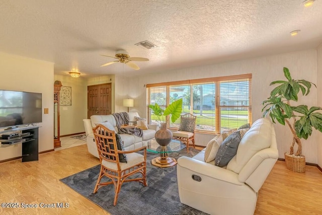 living room featuring a textured ceiling, a ceiling fan, visible vents, baseboards, and light wood finished floors