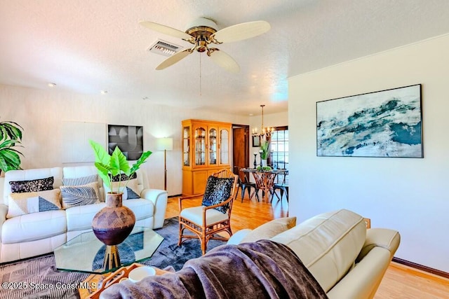 living area with ceiling fan with notable chandelier, visible vents, a textured ceiling, and wood finished floors