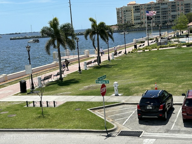 view of home's community with uncovered parking, a water view, and a lawn