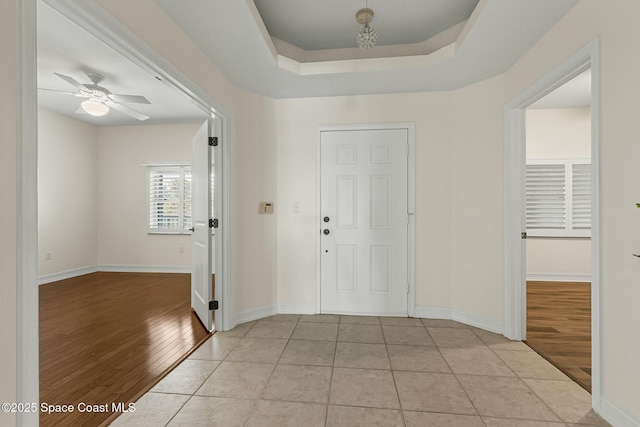 entrance foyer with a tray ceiling, ceiling fan, light wood-style flooring, and baseboards