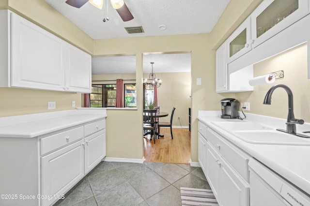 kitchen with a textured ceiling, dishwashing machine, a sink, visible vents, and white cabinetry