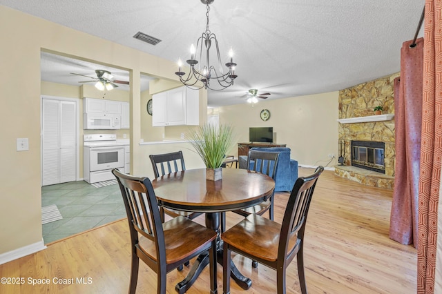 dining space featuring ceiling fan, a fireplace, visible vents, and light wood-style floors