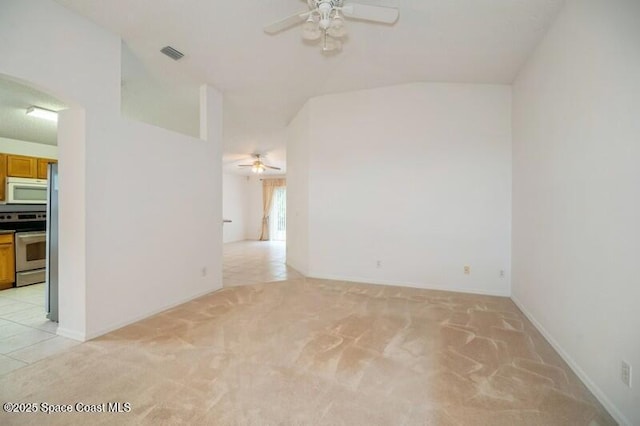 spare room with visible vents, light tile patterned flooring, ceiling fan, vaulted ceiling, and light colored carpet