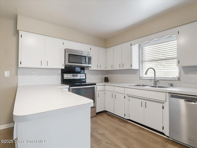 kitchen featuring a sink, white cabinetry, light countertops, appliances with stainless steel finishes, and light wood-type flooring