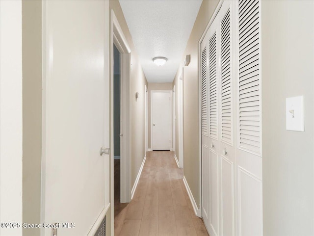 hallway with a textured ceiling, light wood-style flooring, and baseboards