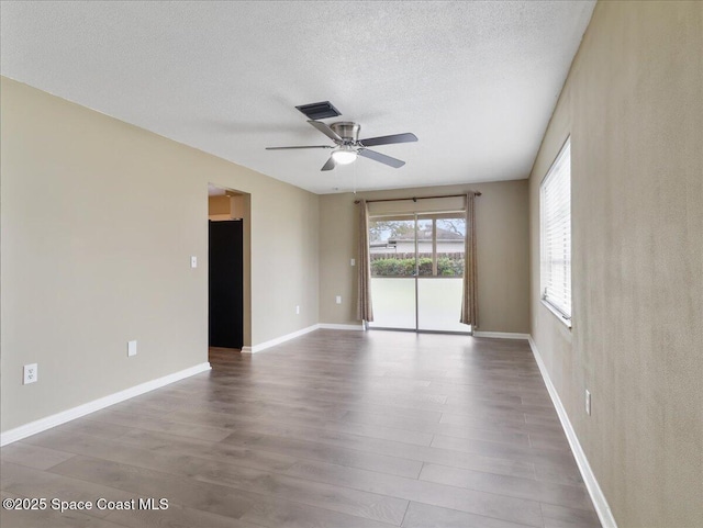 spare room with baseboards, visible vents, ceiling fan, wood finished floors, and a textured ceiling