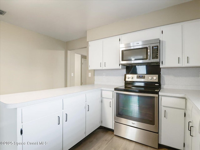 kitchen with appliances with stainless steel finishes, white cabinets, light countertops, and a peninsula