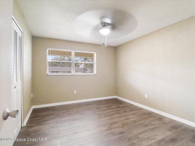 unfurnished bedroom featuring a closet, a ceiling fan, a textured ceiling, wood finished floors, and baseboards