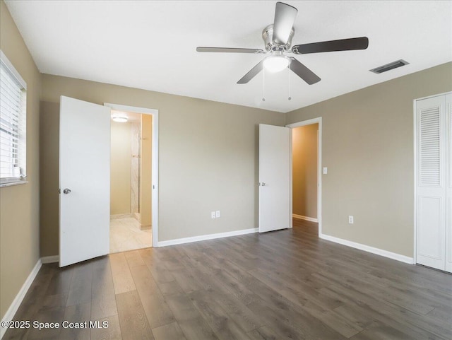 unfurnished bedroom featuring baseboards, visible vents, wood finished floors, ensuite bathroom, and a closet