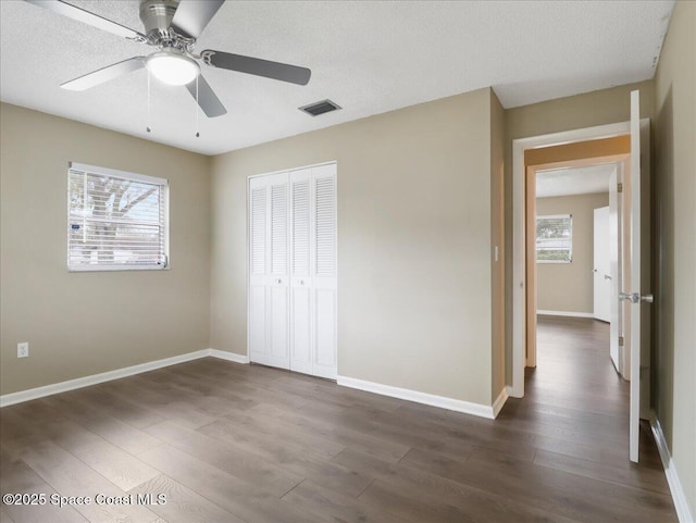 unfurnished bedroom with a closet, dark wood-style flooring, visible vents, and multiple windows