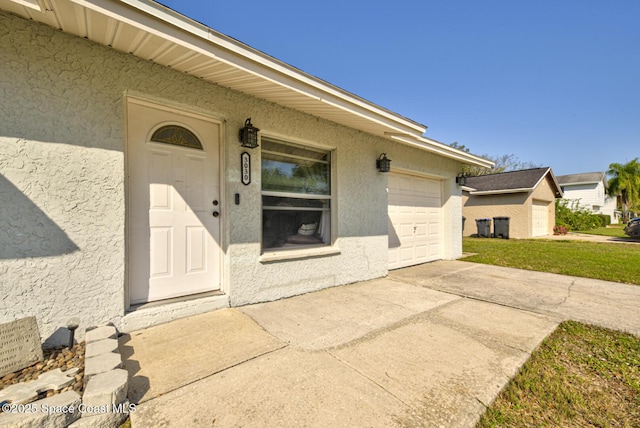 entrance to property featuring concrete driveway, a lawn, an attached garage, and stucco siding