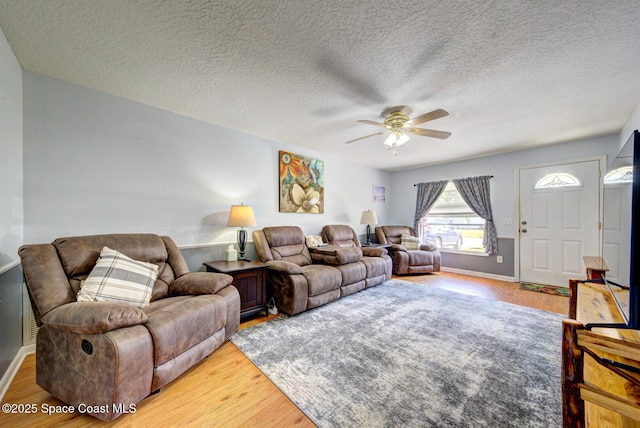 living area with a textured ceiling, wood finished floors, a ceiling fan, and baseboards