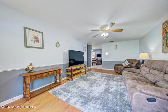 living room featuring a ceiling fan, baseboards, and wood finished floors