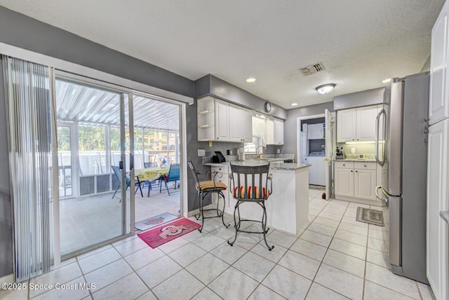 kitchen with washer / clothes dryer, visible vents, freestanding refrigerator, white cabinetry, and a peninsula