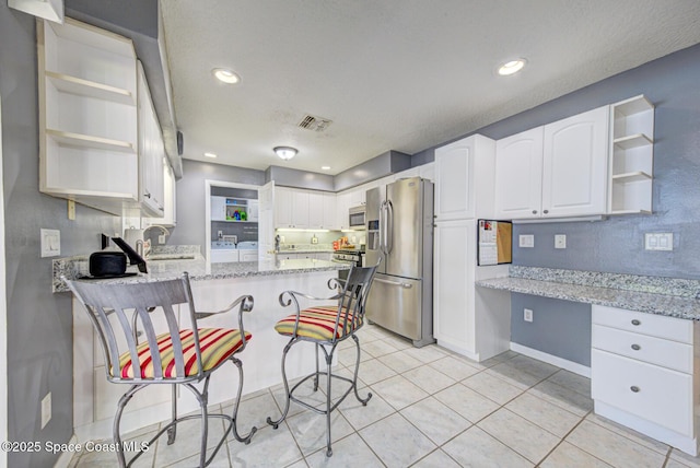 kitchen with light stone counters, a peninsula, appliances with stainless steel finishes, built in study area, and open shelves