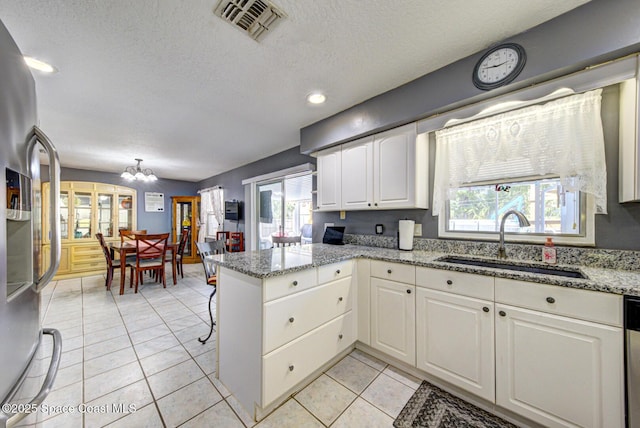 kitchen with visible vents, appliances with stainless steel finishes, white cabinetry, a sink, and a peninsula