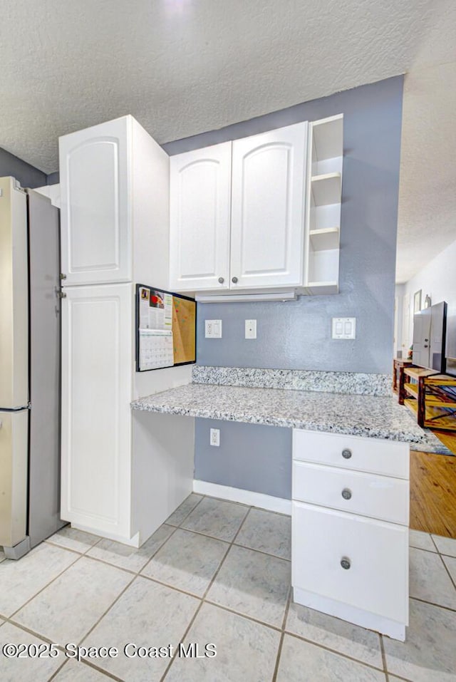 kitchen featuring light tile patterned floors, built in desk, freestanding refrigerator, and white cabinets