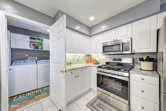 kitchen with a textured ceiling, light stone counters, white cabinetry, washer and dryer, and appliances with stainless steel finishes