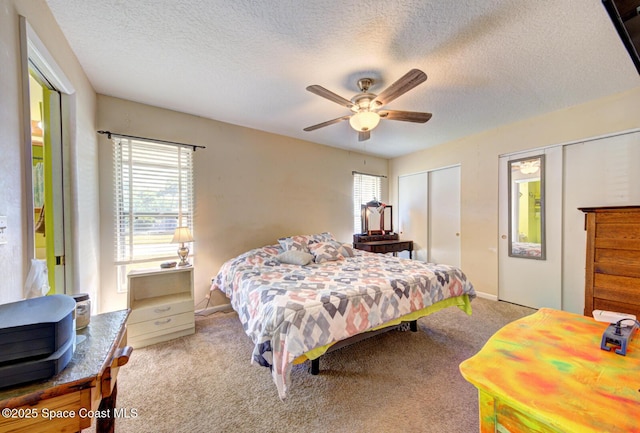 bedroom with a textured ceiling, carpet floors, two closets, and a ceiling fan