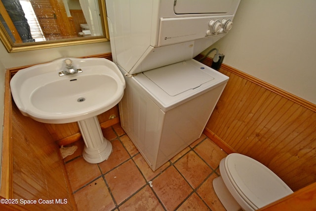 bathroom featuring toilet, wainscoting, wood walls, stacked washing maching and dryer, and tile patterned flooring