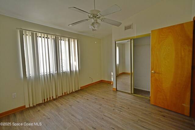 unfurnished bedroom featuring ceiling fan, wood finished floors, visible vents, baseboards, and a closet