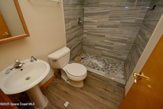 full bath featuring a sink, tiled shower, wood finished floors, and toilet