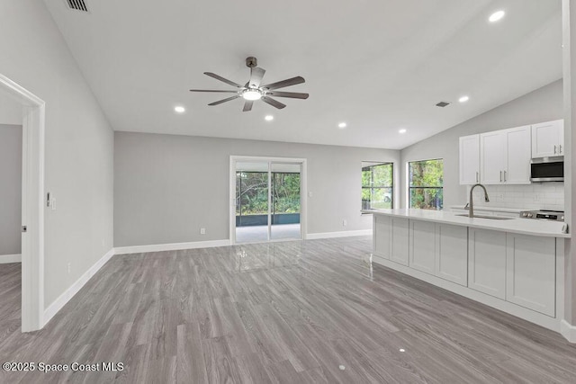 unfurnished living room featuring light wood finished floors, visible vents, baseboards, vaulted ceiling, and recessed lighting