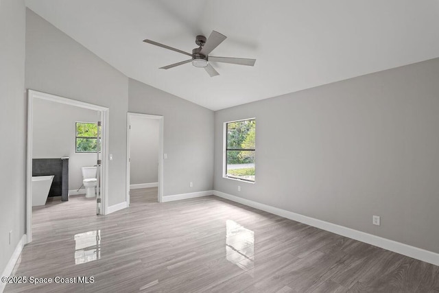 unfurnished bedroom featuring vaulted ceiling, multiple windows, wood finished floors, and baseboards