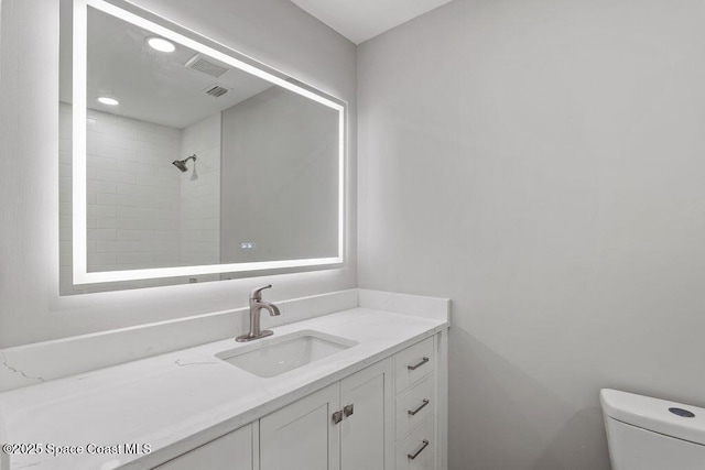 bathroom with visible vents, a tile shower, vanity, and toilet