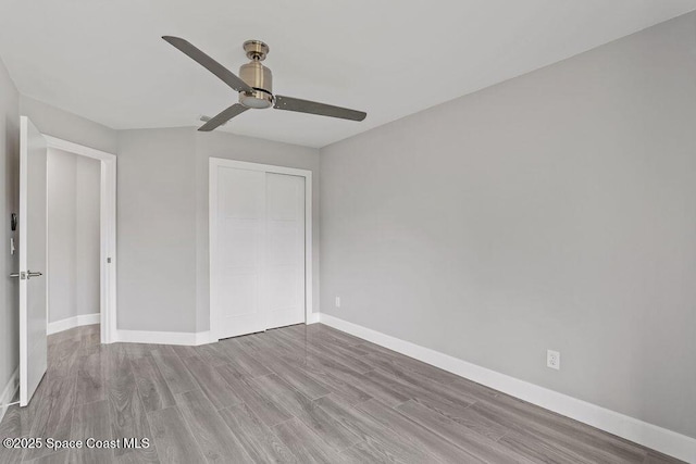 unfurnished bedroom featuring a closet, ceiling fan, baseboards, and wood finished floors