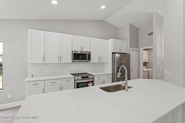 kitchen featuring lofted ceiling, a sink, visible vents, appliances with stainless steel finishes, and washing machine and clothes dryer