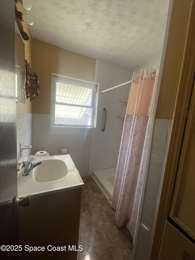 full bathroom featuring a shower with curtain, a wainscoted wall, a textured ceiling, vanity, and tile walls