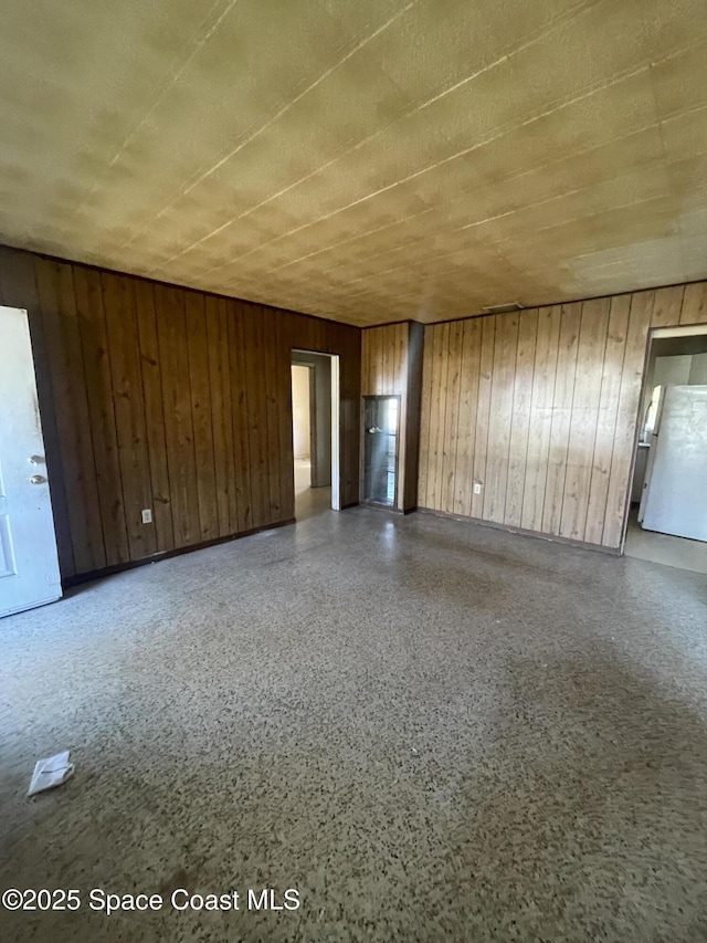 unfurnished room featuring speckled floor and wood walls