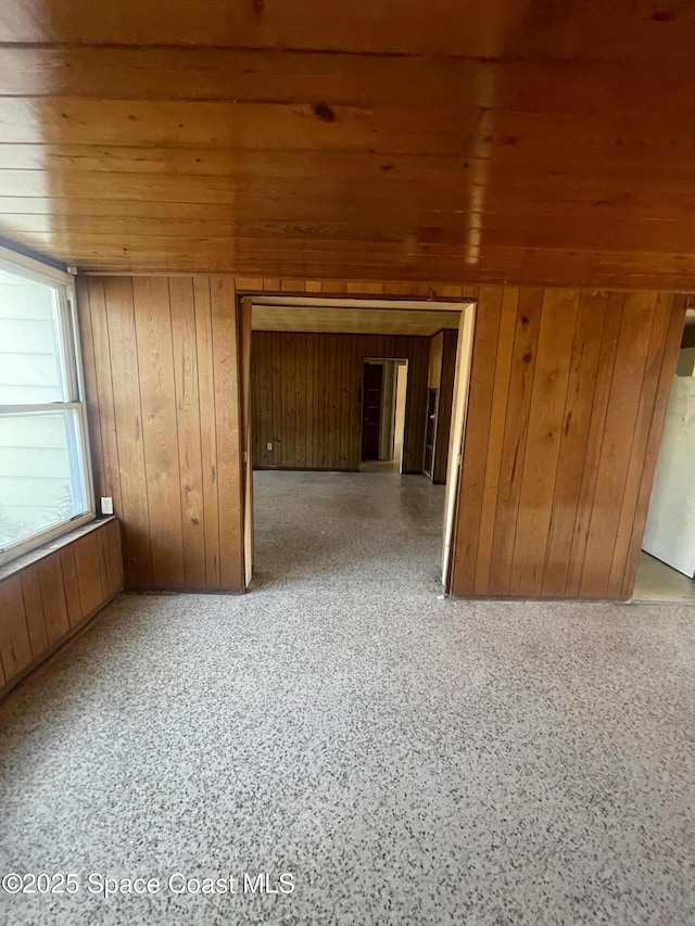 unfurnished room with wooden ceiling, wood walls, and speckled floor