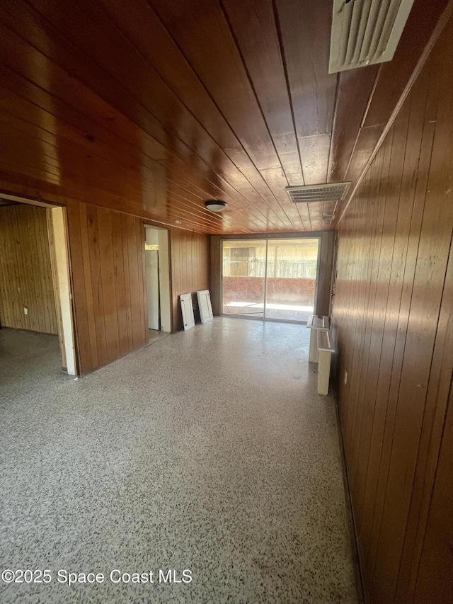 empty room with wooden ceiling, wooden walls, and speckled floor