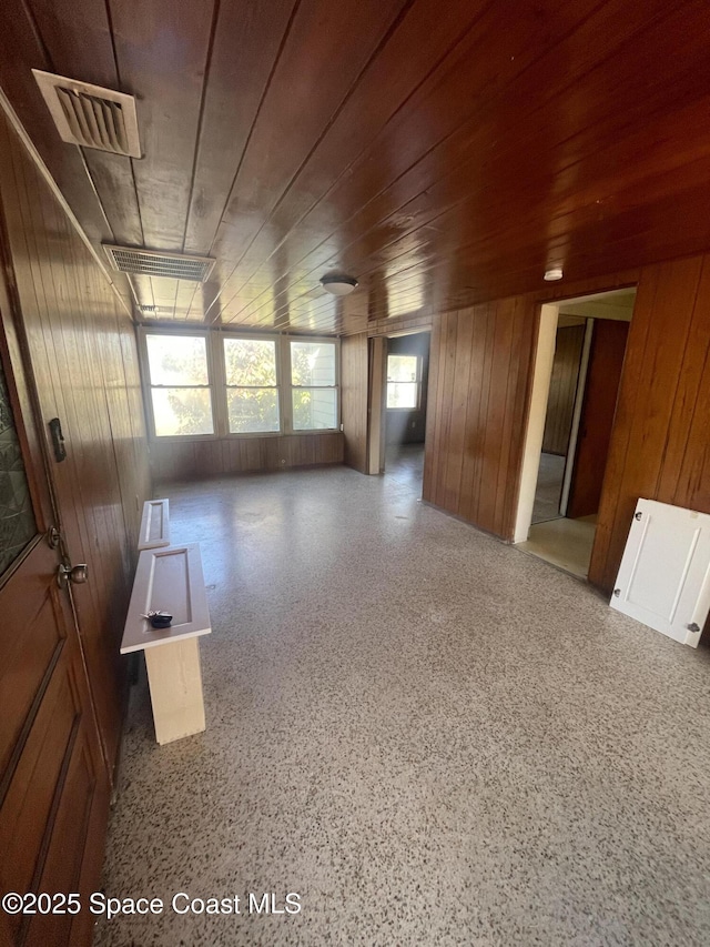 unfurnished room with wood ceiling, speckled floor, visible vents, and wooden walls