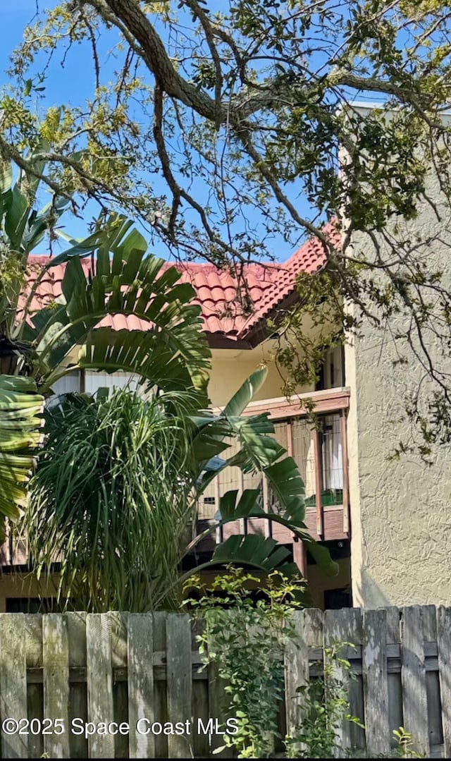 view of side of property featuring fence, a tile roof, and stucco siding