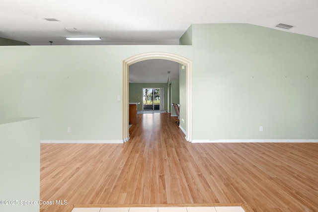 unfurnished room featuring light wood-type flooring, baseboards, arched walkways, and lofted ceiling