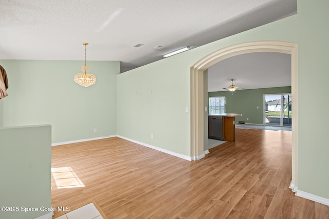 empty room with light wood-style floors, arched walkways, a textured ceiling, and baseboards