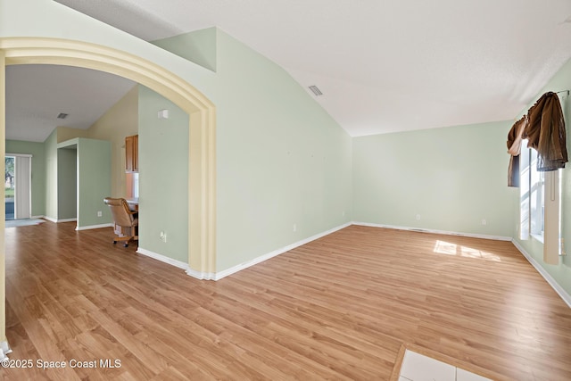 unfurnished room featuring vaulted ceiling, arched walkways, light wood-style flooring, and baseboards