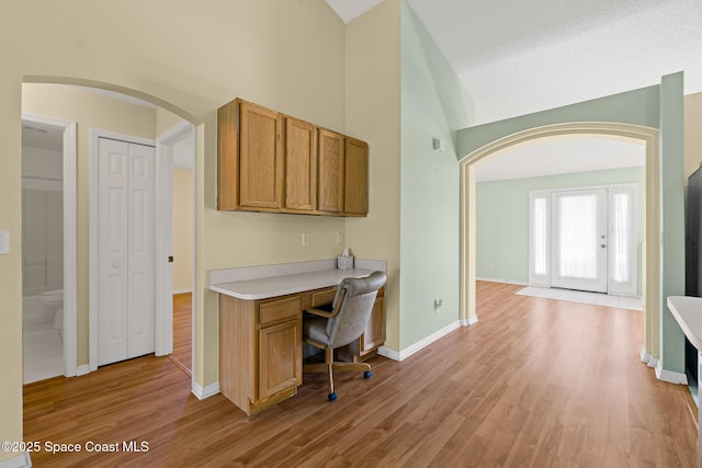 home office featuring arched walkways, high vaulted ceiling, baseboards, light wood-type flooring, and built in study area