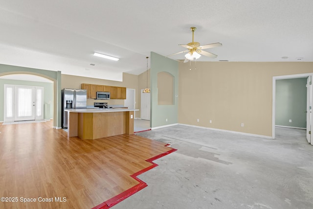 kitchen with arched walkways, stainless steel appliances, light countertops, open floor plan, and vaulted ceiling