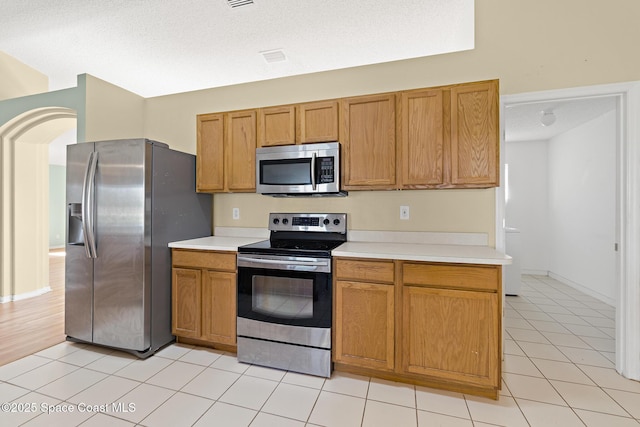 kitchen featuring a textured ceiling, stainless steel appliances, light countertops, and brown cabinets