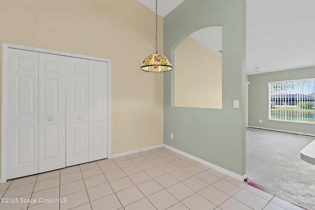 unfurnished dining area featuring lofted ceiling, light tile patterned floors, baseboards, and arched walkways