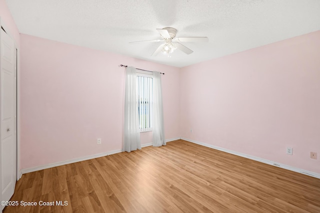 unfurnished room with ceiling fan, light wood finished floors, a textured ceiling, and baseboards