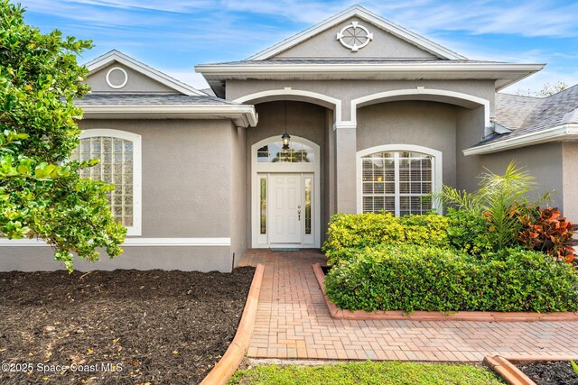 entrance to property with a shingled roof and stucco siding